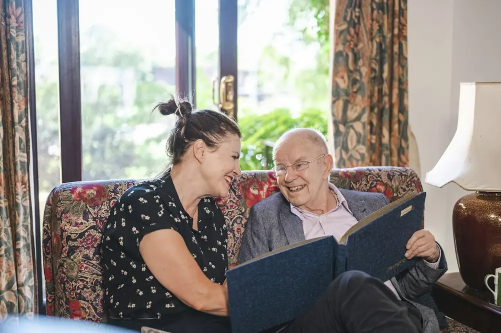 A woman and an older man reading together on a sofa at home